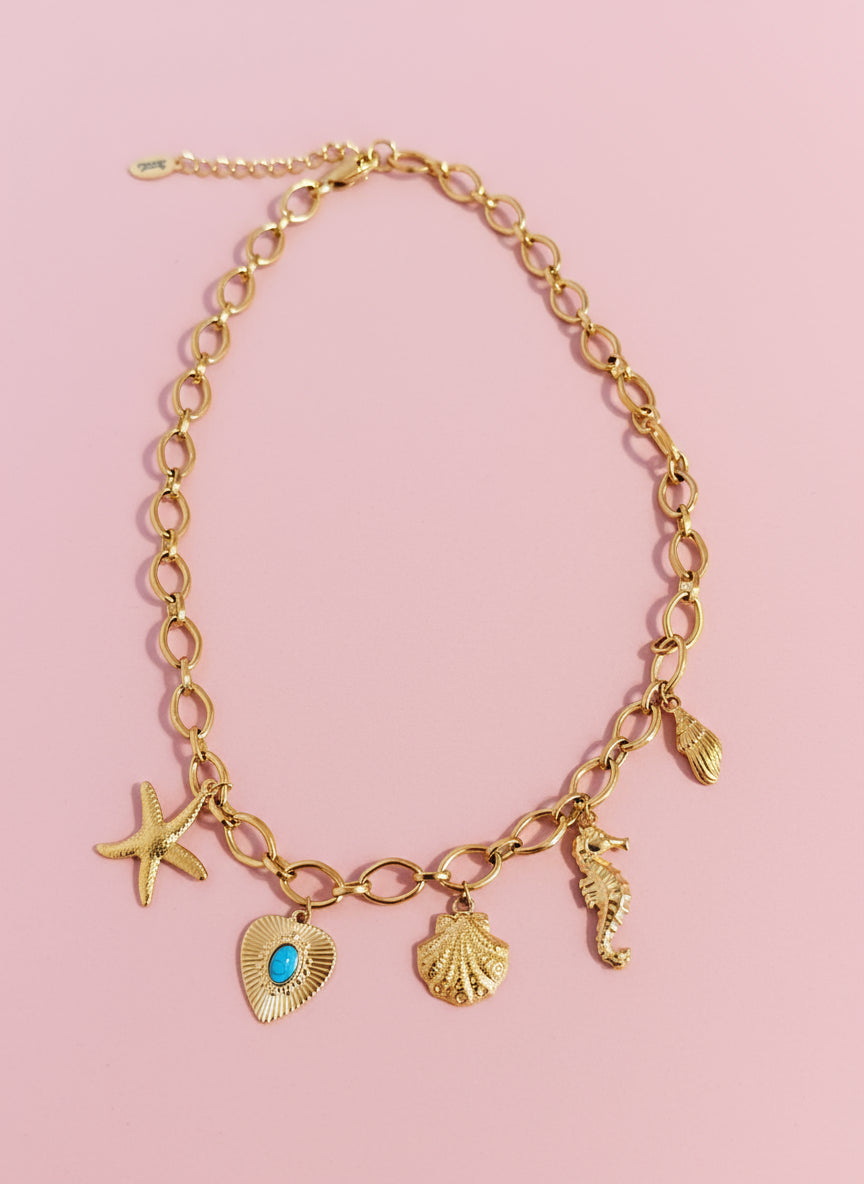 A gold stainless steel charm necklace with various charms including a starfish, a clam shell, a seahorse, a turquoise heart, and a conch shell.