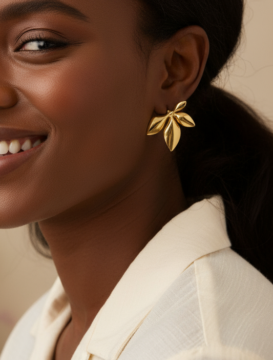 Close-up of a woman wearing gold leaf earrings with a neutral background