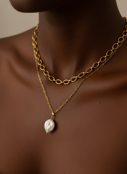 Gold chain necklace with a pearl pendant on a person's neck against a neutral background