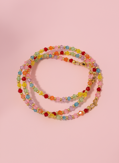 A multicolored beaded bracelet with a variety of colorful glass crystals and gold beads, displayed on a shell-like surface.