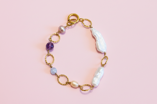Bracelet with gold links, pearls, and amethysts on a pink background