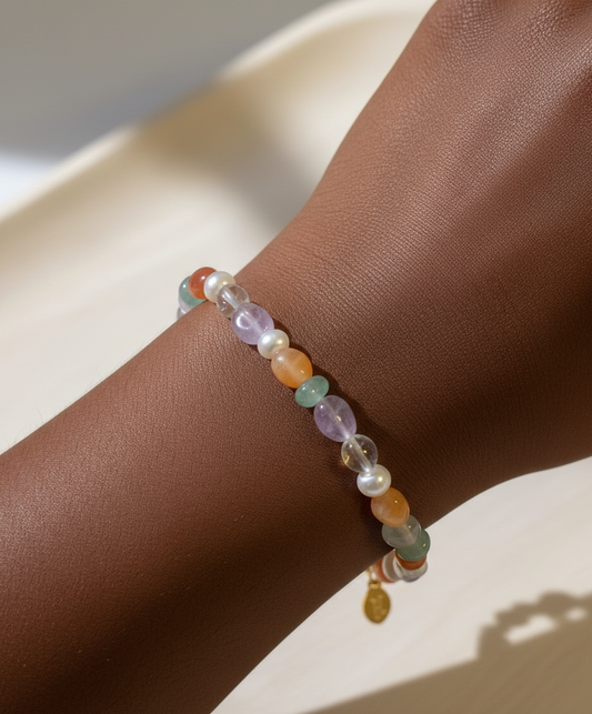 A multicolored gemstone bracelet with amethyst, fire agate, and green aventurine, featuring freshwater pearls and clear beads, on a wooden surface.