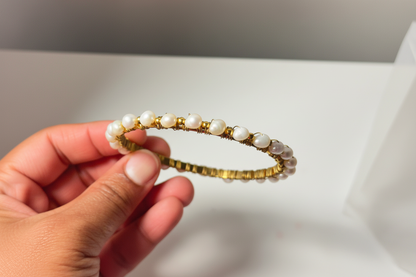 Hand holding a beaded bracelet with gold accents against a neutral background