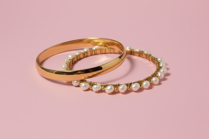 Two gold bangles with pearl accents on a light background