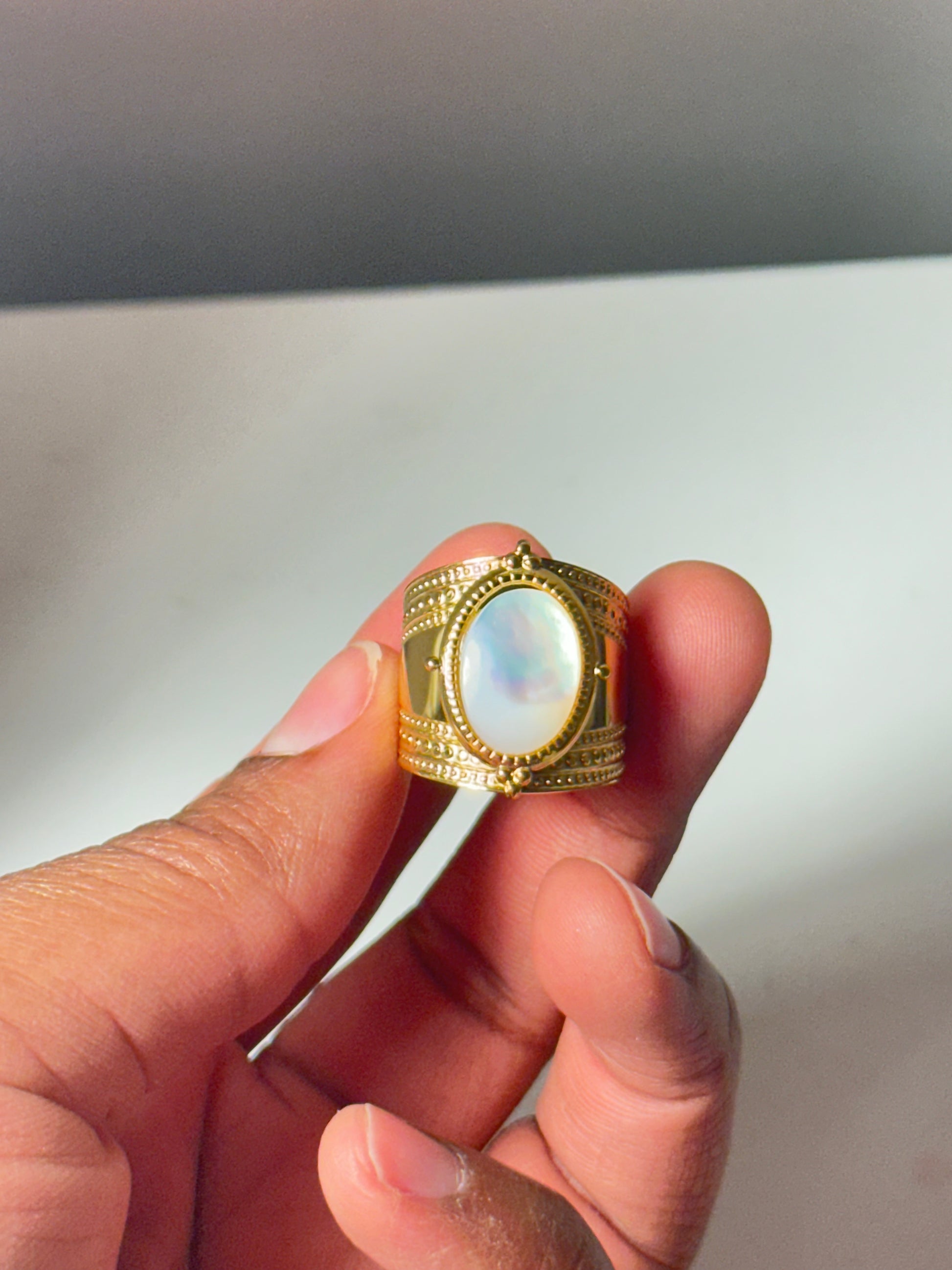 Gold ring with a large gemstone held between fingers against a neutral background