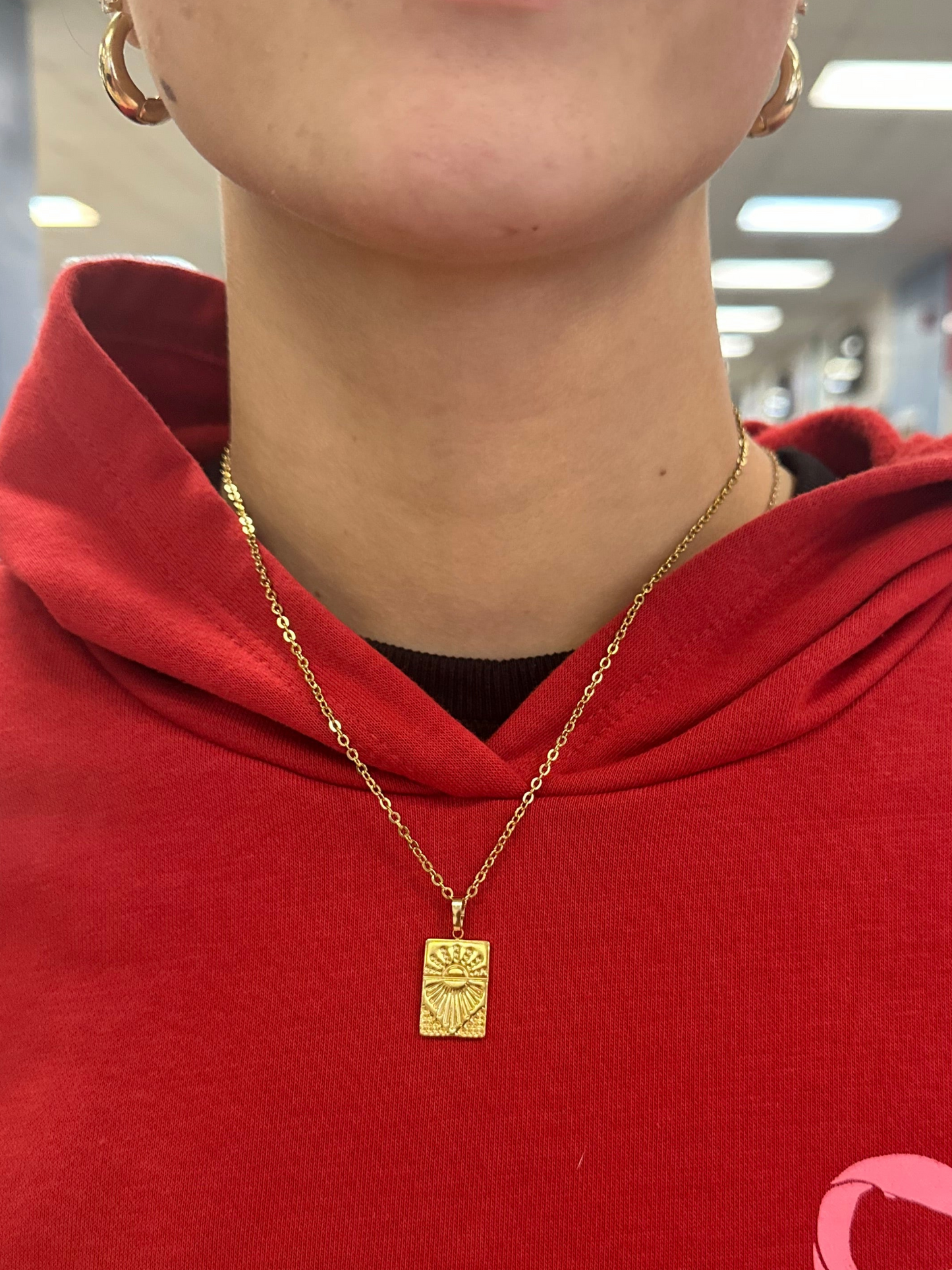 Person wearing a red garment with a pink bow design, gold necklace, and visible jewelry.